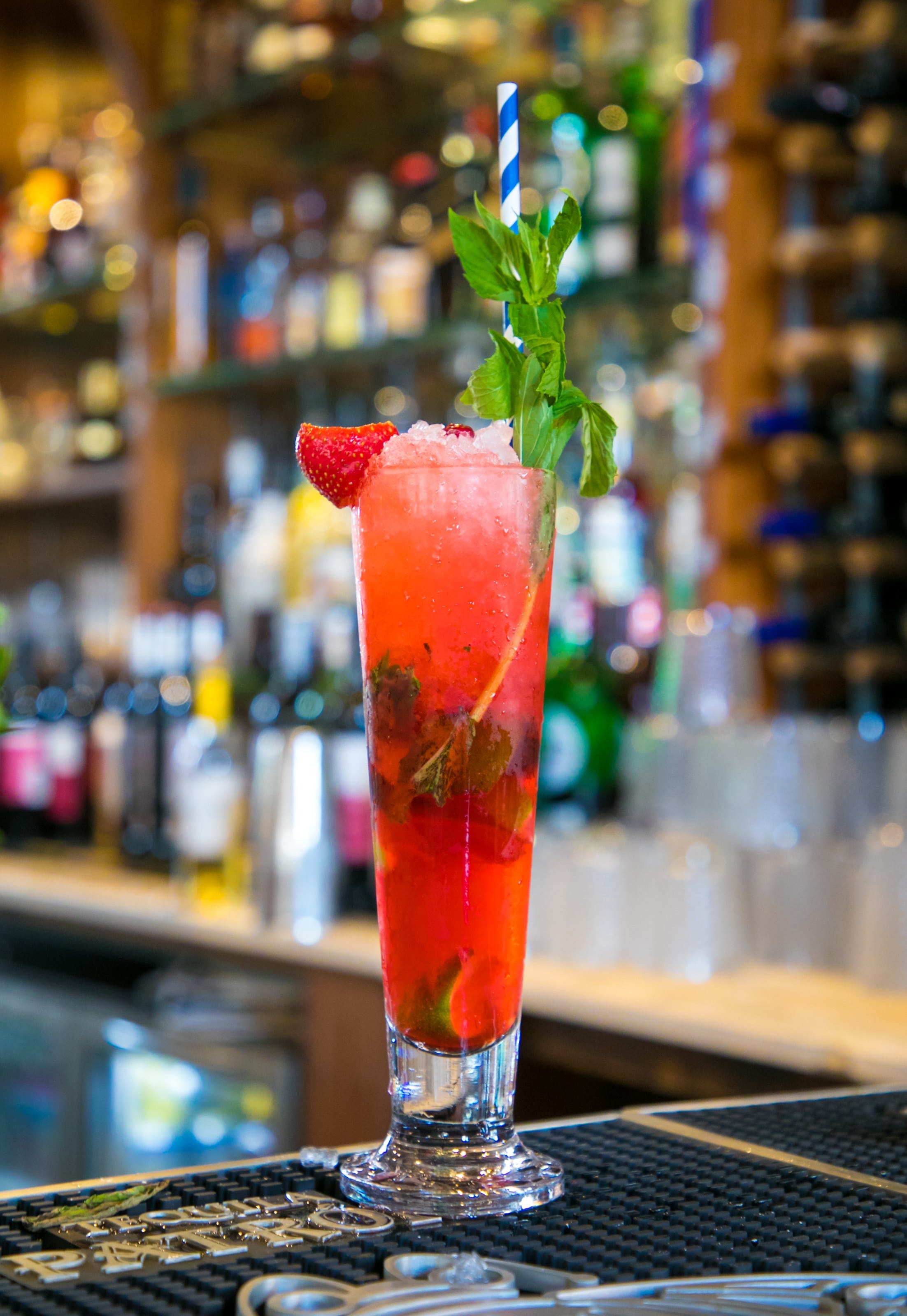A tall red cocktail with mint on a bar