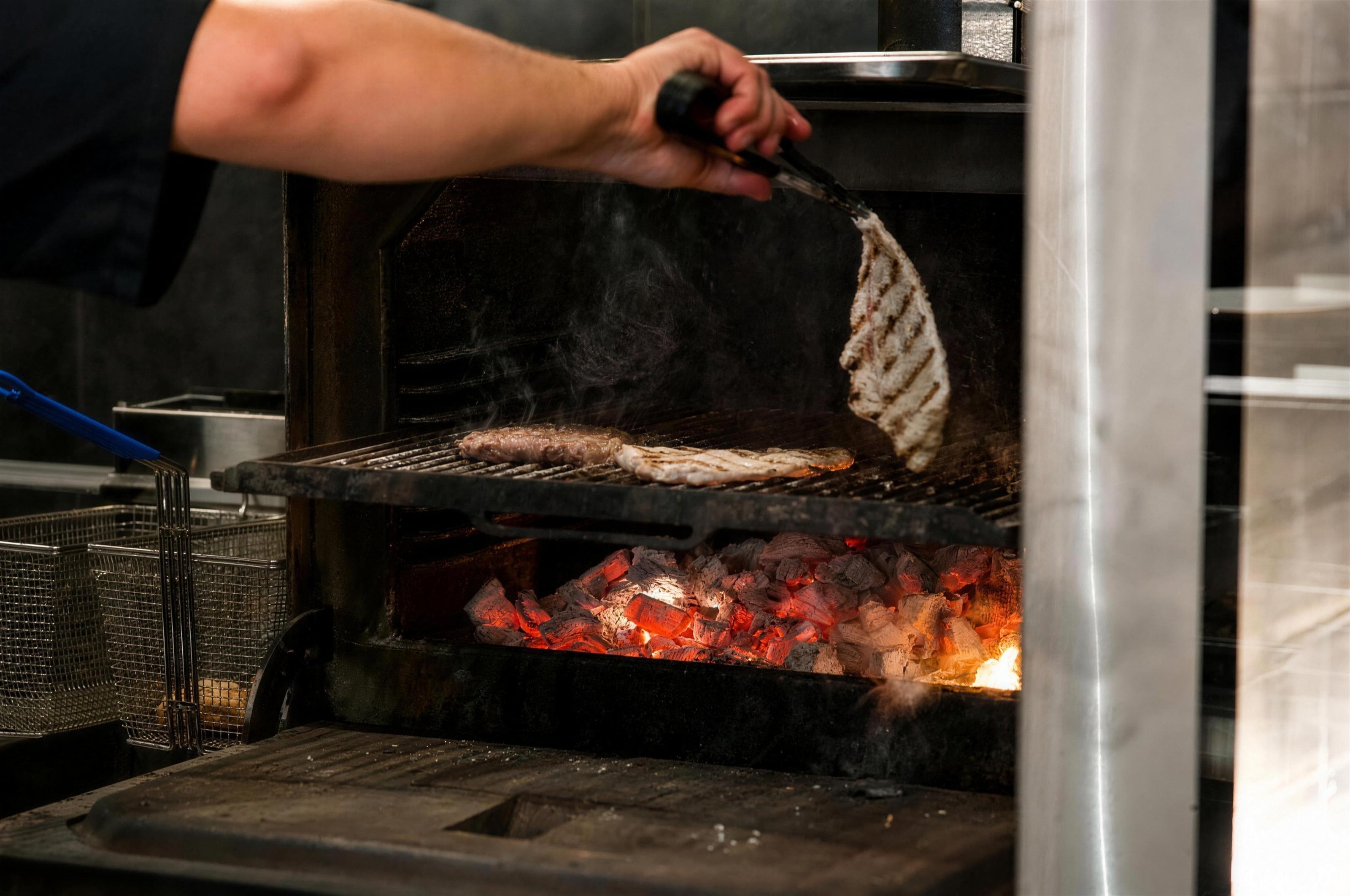 A chef turning meat over a charcoal grill